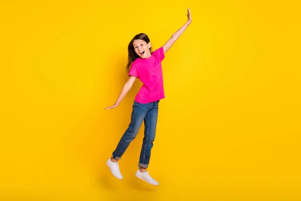 Foto de funky desportivo feliz menina salto desfrutar de fim de semana desgaste rosa t-shirt jeans tênis isolado cor amarela fundo — Fotografia de Stock