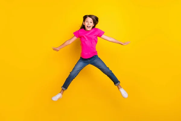 Fotografie bláznivé aktivní veselá dívka skok otevřená ústa nosit růžové tričko džíny tenisky izolované žlutá barva pozadí — Stock fotografie