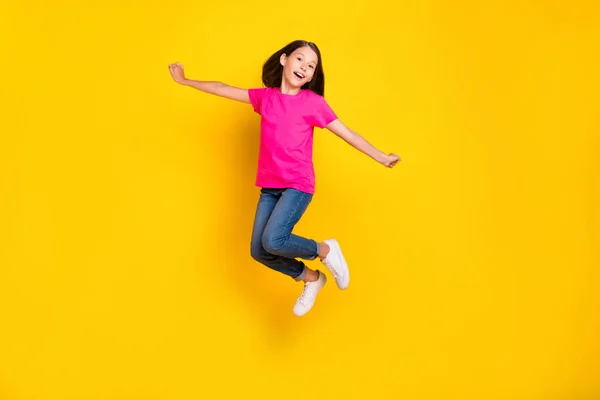 照片中有趣的积极女孩跳无忧无虑的飞行穿着粉色T恤牛仔裤运动鞋孤立的黄色背景 — 图库照片