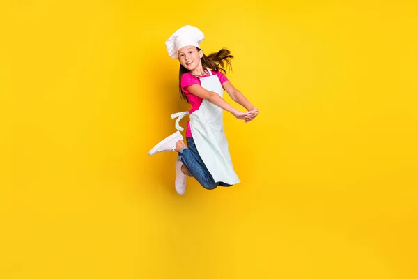 Foto di attiva adorabile bambina salto tenere braccia indossare grembiule cap scarpe isolato colore giallo sfondo — Foto Stock