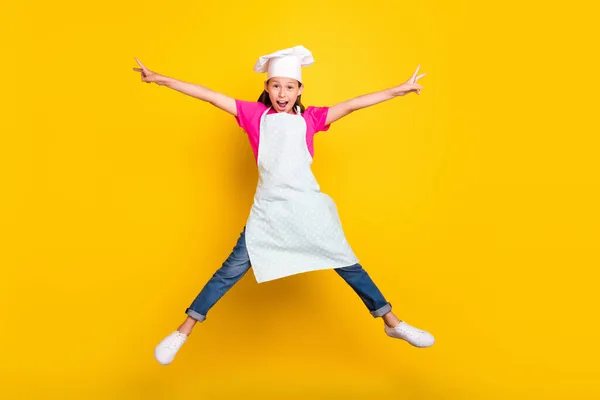 Foto av energiska bekymmersfri liten flicka hoppa upp händerna stjärna form bära förkläde mössa skor isolerad gul färg bakgrund — Stockfoto