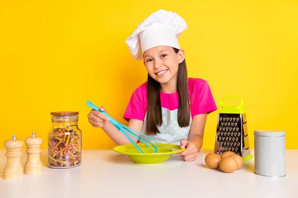Foto di allegro popolare blog chef bambina mix uova frittata indossare grembiule tappo isolato colore giallo sfondo — Foto Stock