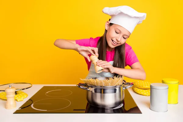 Foto di fiducioso allegra bambina tenere pepe casella spezie spaghetti indossare tappo grembiule isolato colore giallo sfondo — Foto Stock