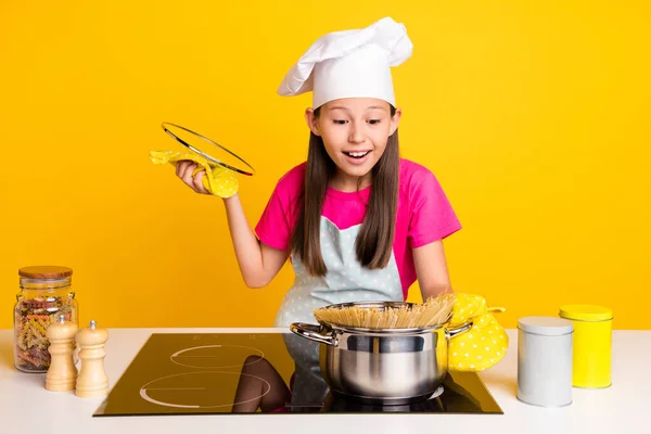 Photo of excited surprised little girl cook pasta check process wear glove apron cap isolated yellow color background