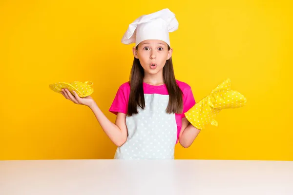 Foto di indiziato eccitato bambina rimanere tavolo togliere i guanti indossare bianco tappo grembiule isolato colore giallo sfondo — Foto Stock