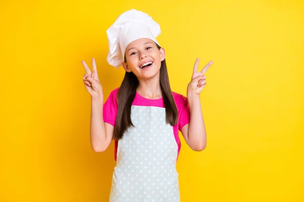 Foto di piccola signora amichevole eccitato mostrano due v-segni indossare bianco grembiule cappello isolato colore giallo sfondo — Foto Stock