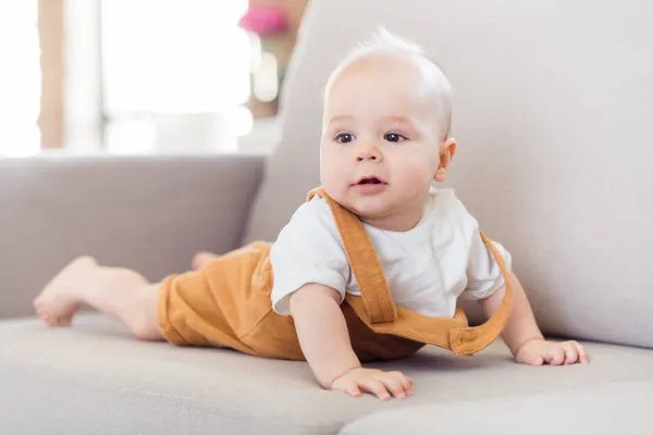 Foto de niño pequeño lindo curioso bebé cama sofá cómodo mirar lejos usar tirantes casa interior — Foto de Stock