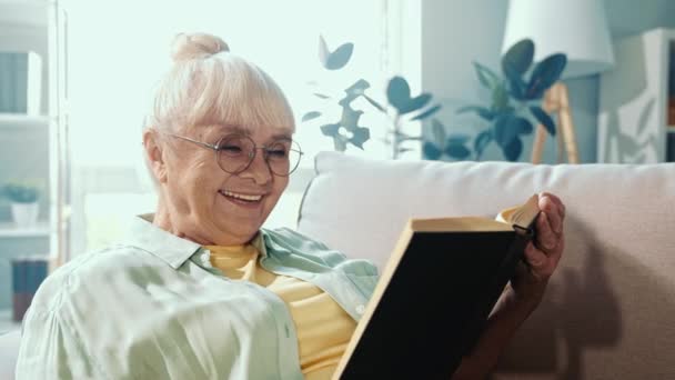 Positiv froh schöne alte Dame sitzt Couch lesen interessanten Roman — Stockvideo