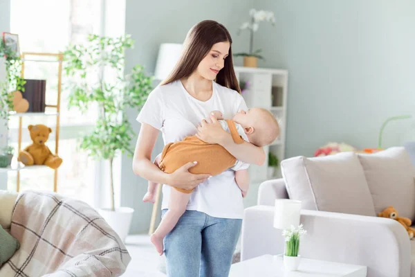 Fotografie půvabné roztomilé matky oblečené bílé tričko držící ruce spící dítě uvnitř vnitřního apartmánu pokoj — Stock fotografie