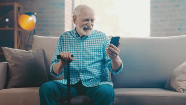 Abuelo sentarse sofá escribiendo mensaje de teléfono distancia noticias de navegación — Vídeos de Stock