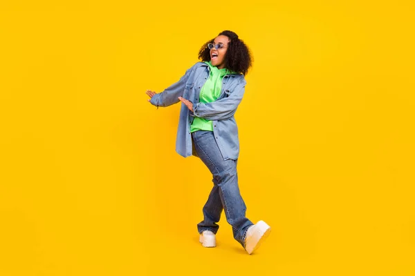 Fénykép elég vonzó afro nő visel farmer kabát sötét szemüveg mosolygós tánc elszigetelt sárga szín háttér — Stock Fotó