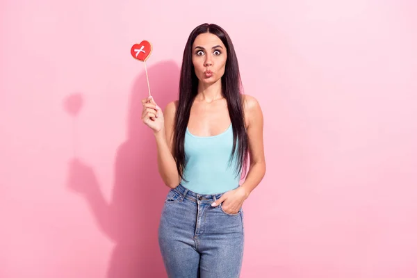 Портрет привлекательной комической девушки, держащей сладкие сердечные конфеты, посылающие воздушный поцелуй изолирован на розовом пастельном фоне — стоковое фото
