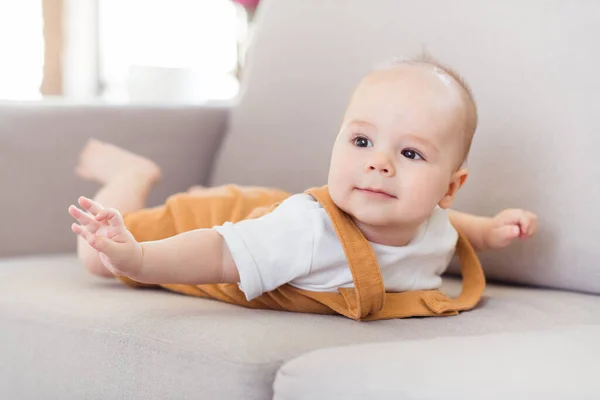 Foto de niño pequeño bastante lindo usar naranja sofá acostado en general dentro de la habitación de la casa interior — Foto de Stock