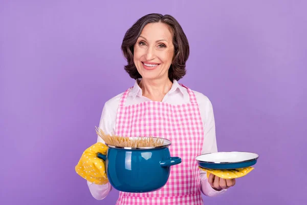 Foto van mooie fornuis wit leeftijd dame houd pan dragen wit shirt schort geïsoleerd op paarse kleur achtergrond — Stockfoto