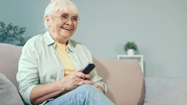 Позитивный смешной бабушкин диван расслабляет смотреть телевизионное комедийное шоу смех — стоковое видео