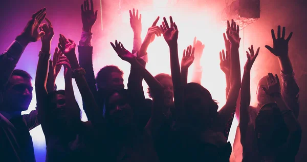Fénykép a vidám fiatalok, amelyek vállalati diszkó alkalom tánc emelje fel a kezét a diszkó színes modern fények — Stock Fotó