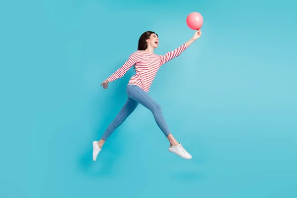 Повна довжина вигляд тіла приваблива весела дівчина стрибає тримаючи м'яч, розважаючись ізольовано на яскраво-синьому кольоровому фоні — стокове фото