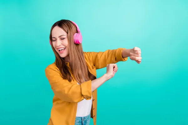 Foto de señora madura encantadora brillante usar camisa amarilla bailando disfrutando de auriculares musicales sonriendo aislado color turquesa fondo — Foto de Stock