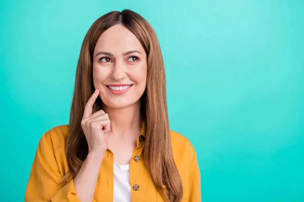 Photo of charming tricky young woman dressed yellow shirt smiling looking empty space finger cheek isolated teal color background — Stock Photo, Image