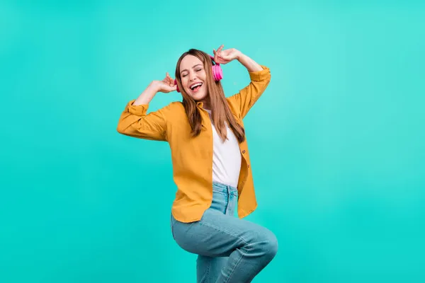 Foto de mujer joven bastante dulce vestida camisa amarilla sonriendo escuchando canciones auriculares bailando aislado color verde azulado fondo — Foto de Stock