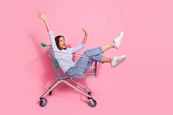 Foto de menina bonita funky vestido branco jumper tacking selfie dispositivo moderno ter divertido carrinho de compras isolado cor de fundo rosa — Fotografia de Stock