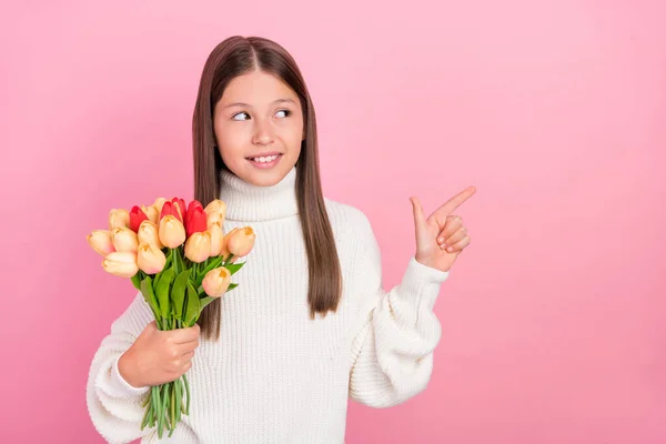 Фото сладкой блестящей девушки носить белый свитер улыбаясь указывая на пустое пространство, держа тюльпаны кучу изолированных розовый цвет фона — стоковое фото