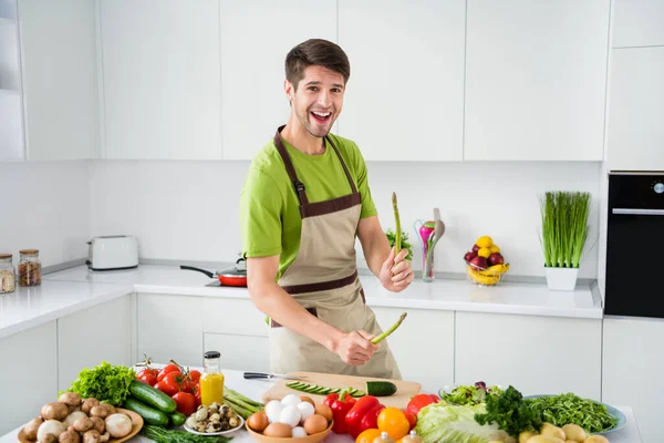 Фотопортрет молодого чоловіка, який готує страву зі спаржею, сміється на кухні — стокове фото