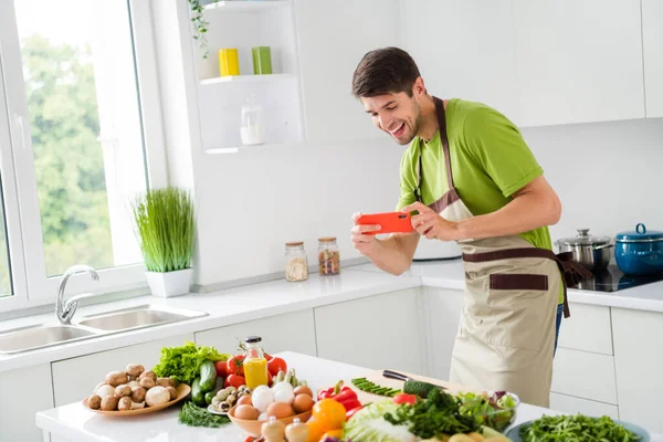 Портрет привабливого фанк-веселого хлопця, який готує свіжий смачний салат з їжею, весело роблячи фотографії на домашній кухні в приміщенні — стокове фото