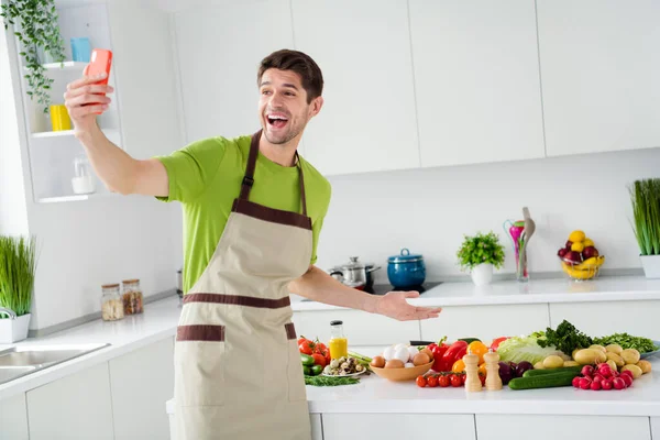 Портрет привабливого веселого хлопця, який готує свіжий салат з їжею, розважається, приймаючи собі гарний настрій на домашній кухні в приміщенні — стокове фото