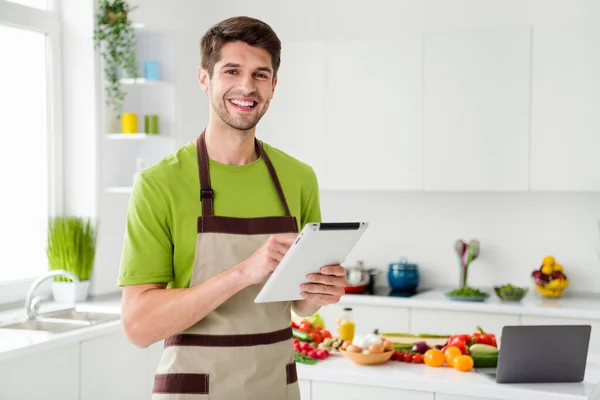 Foto retrato jovem em avental mantendo tablet sorrindo na cozinha — Fotografia de Stock