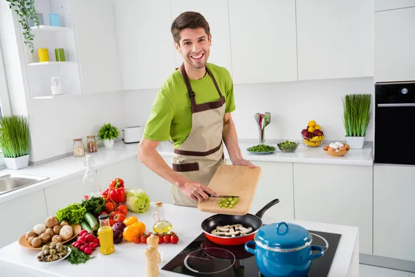 Портрет привабливого веселого хлопця, який готує свіжий обід смачний гурман, додаючи інгредієнт на домашній кухні в приміщенні — стокове фото