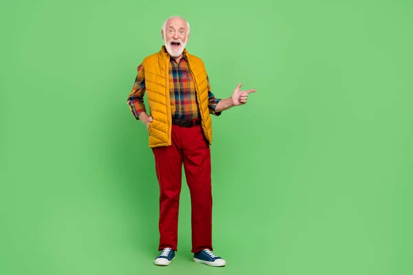 Foto van charmante onder de indruk senior heer dragen gele vest wijzende vinger lege ruimte glimlachen geïsoleerde groene kleur achtergrond — Stockfoto