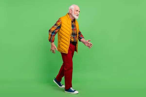 Foto van vrolijke positieve senior gentleman dragen geel vest lopen op zoek lege ruimte glimlachen geïsoleerde groene kleur achtergrond — Stockfoto
