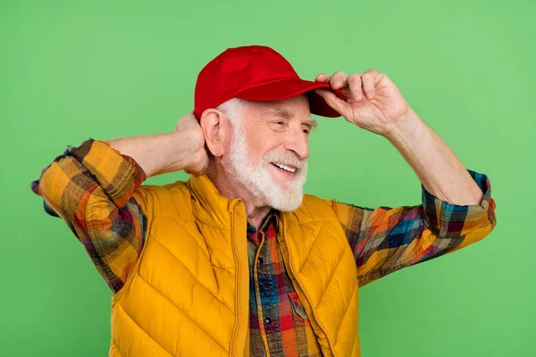 Yakışıklı, hoş, son sınıf beyefendinin fotoğrafı sarı yelek giyip, kırmızı başlık takıp boş boş boş bakıp, izole edilmiş yeşil bir arka plan gülümsüyor. — Stok fotoğraf