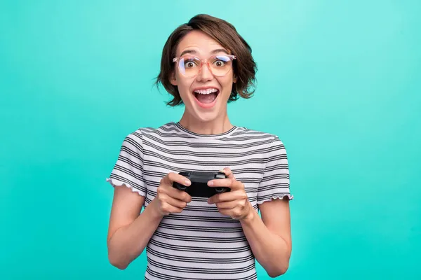 Foto van mooie millennial brunette dame playstation dragen brillen gestreept t-shirt geïsoleerd op teal kleur achtergrond — Stockfoto