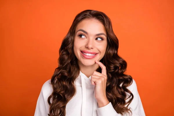 Foto de jovem alegre menina dedo toque queixo ideia pensativa olhar olhar vazio espaço isolado sobre cor laranja fundo — Fotografia de Stock