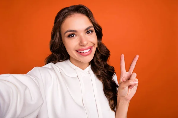 Video blogcusu, turuncu arka planda izole edilmiş barış sembolü gösteren neşeli genç bir kızın fotoğrafı — Stok fotoğraf