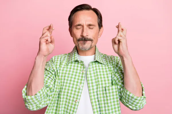 Foto van ongelukkige zorgen leeftijd man dragen groen geruite shirt gesloten ogen vingers gekruist geïsoleerd licht pastel roze kleur achtergrond — Stockfoto