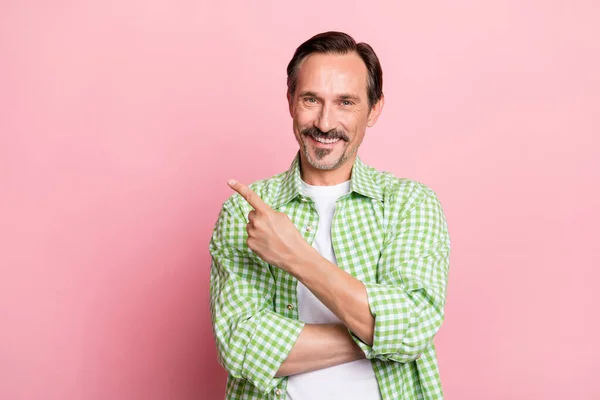 Foto de confiante bonito idade homem desgaste verde xadrez camisa apontando dedo vazio espaço sorrindo isolado luz pastel cor de rosa fundo — Fotografia de Stock