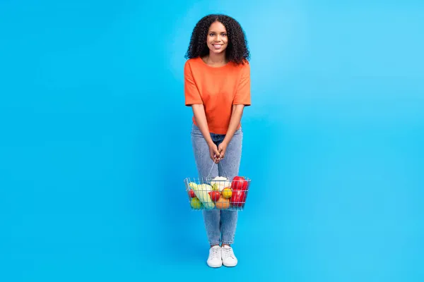 Genç afro kadının tam boy fotoğrafı mutlu pozitif gülüş süpermarketi mavi arka planda izole edilmiş yiyecek satın alıyor. — Stok fotoğraf