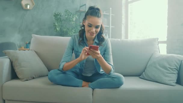 Positieve dromerige dame zitten comfortabele bank chatten telefoon sms — Stockvideo