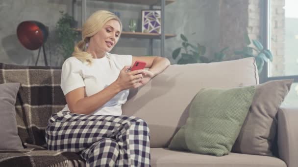 Позитивний блогер леді сидить затишний диван тримає телефонний прокрутка соціальних медіа — стокове відео