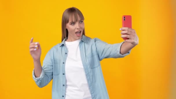 Позитивный фанки влиятельный леди держать телефон сделать селфи шоу жесты — стоковое видео