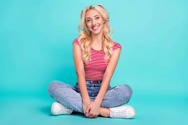 魅力的な光沢のある若い女性の写真縞模様のTシャツの床に座って足を交差笑顔孤立ターコイズ色の背景 — ストック写真