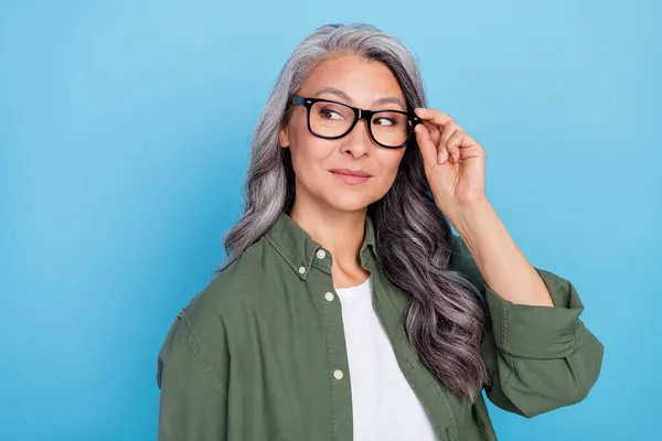 Fénykép aranyos idősebb szürke frizura hölgy néz üres tér viselet szemüveg khaki ing elszigetelt kék színű háttér — Stock Fotó