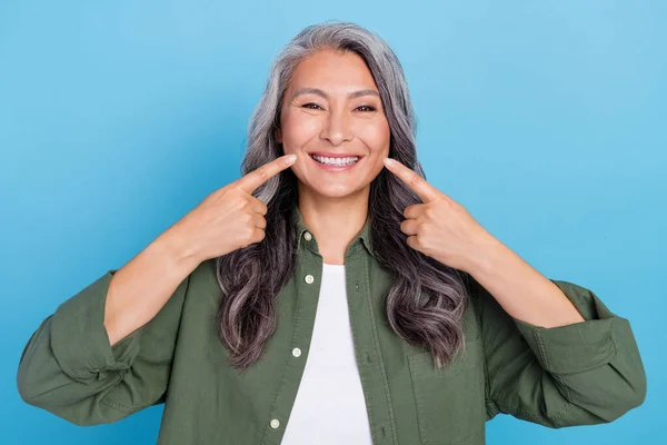 Foto de señora de pelo gris envejecido divertido indican dientes usan camisa caqui aislado en fondo de color azul —  Fotos de Stock