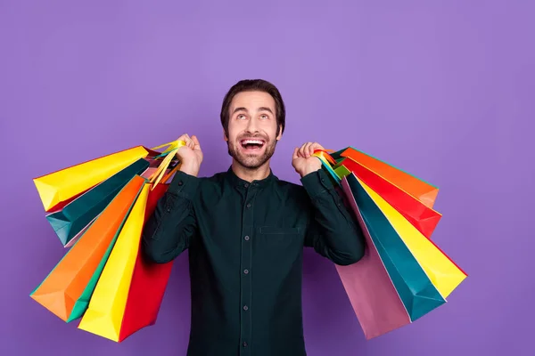 Photo of funky attractive young man wear smart casual outfit looking up empty space holding shopping bags isolated purple color background — Stock Photo, Image