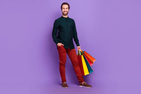 Zdjęcie dość funky młody człowiek nosić inteligentny strój casual uśmiechnięty spacery gospodarstwa zakupy okazje odizolowane fioletowy kolor tła — Zdjęcie stockowe