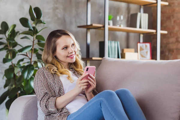 Портрет привлекательной веселой девушки, сидящей на диване, проводящей свободное время с помощью гаджета приложение 5g в интерьере промышленного стиля в помещении — стоковое фото