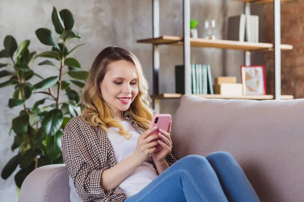 Фотопортрет молодая женщина улыбается сидя на диване просматривая интернет мобильный телефон — стоковое фото